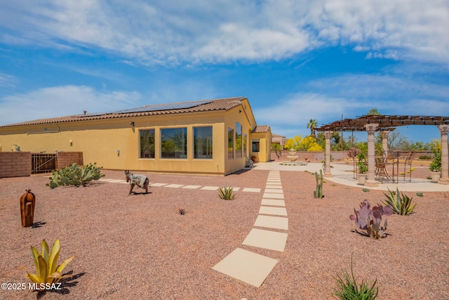rear view of property featuring roof mounted solar panels, a patio, stucco siding, a pergola, and fence
