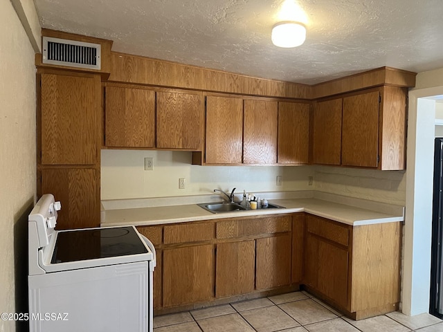 kitchen with brown cabinetry, a textured ceiling, a sink, light countertops, and electric stove