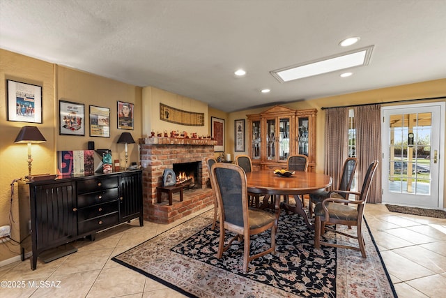 dining space featuring recessed lighting, lofted ceiling with skylight, a brick fireplace, and light tile patterned floors