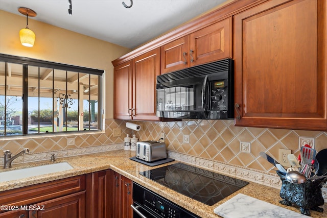 kitchen featuring decorative backsplash, light stone countertops, a sink, black appliances, and hanging light fixtures