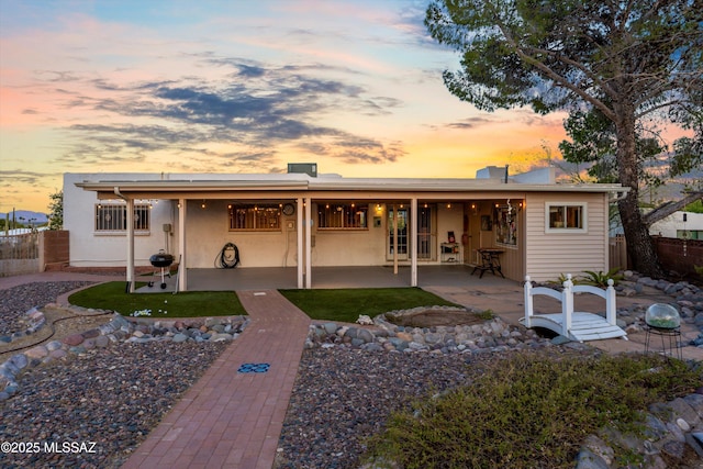 rear view of house with a patio, fence, and stucco siding