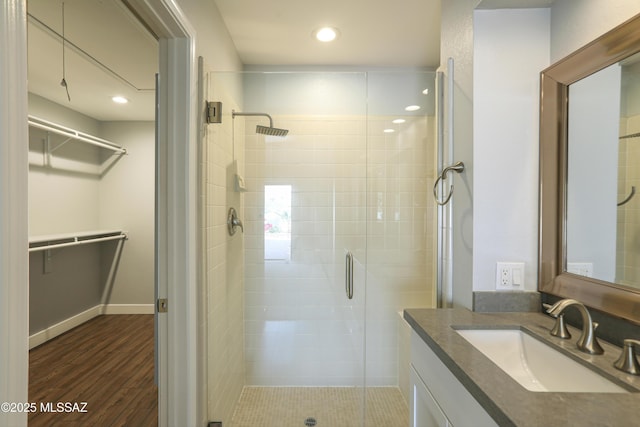 bathroom featuring a walk in closet, vanity, recessed lighting, wood finished floors, and a stall shower