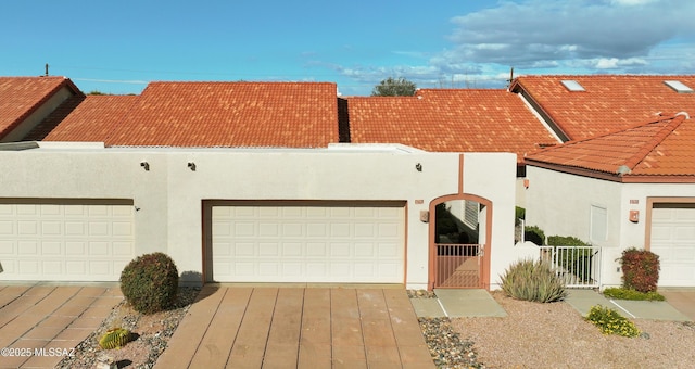 view of front of home with a tiled roof, an attached garage, a gate, and stucco siding