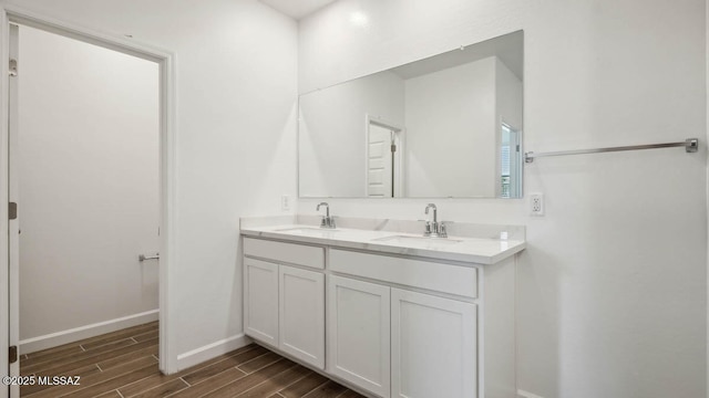 bathroom with baseboards, double vanity, wood finish floors, and a sink