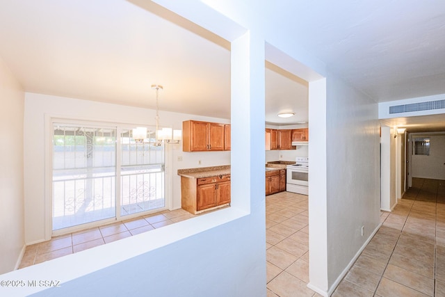 kitchen featuring brown cabinetry, visible vents, light tile patterned floors, electric range, and a notable chandelier