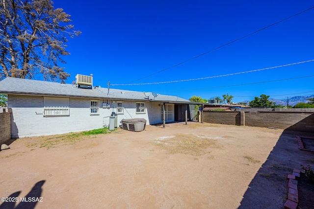 back of property with central AC, brick siding, and fence