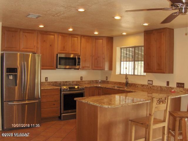 kitchen with a peninsula, a sink, stainless steel appliances, ceiling fan, and light stone counters