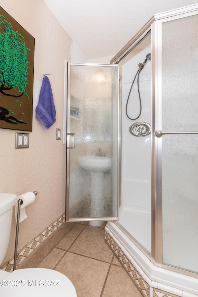 bathroom featuring a stall shower, toilet, a textured wall, and tile patterned floors