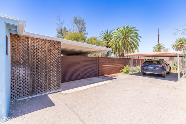 view of parking / parking lot with fence and a carport