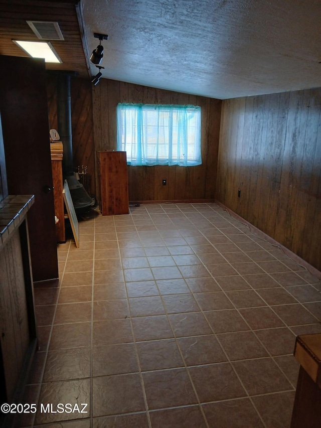 unfurnished living room featuring tile patterned floors, a textured ceiling, visible vents, and wooden walls