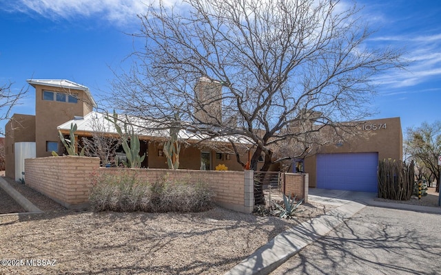 adobe home with an attached garage, driveway, stucco siding, a fenced front yard, and a chimney