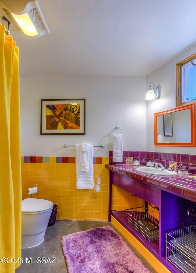 bathroom featuring a sink, wainscoting, tile walls, and toilet