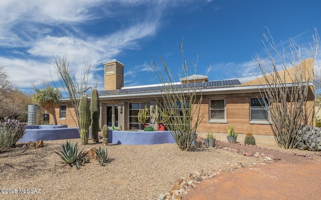 back of property featuring a chimney and solar panels