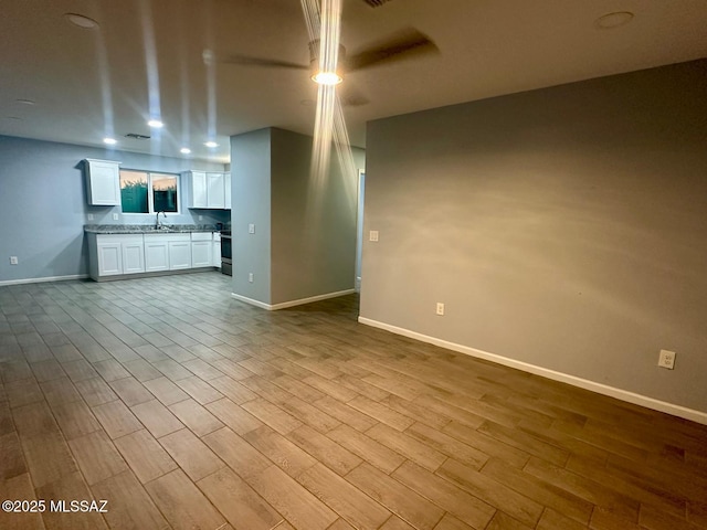 unfurnished living room featuring recessed lighting, baseboards, ceiling fan, a sink, and wood finished floors