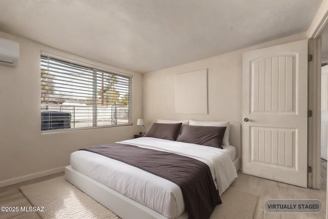 bedroom featuring baseboards, a wall unit AC, and wood finished floors
