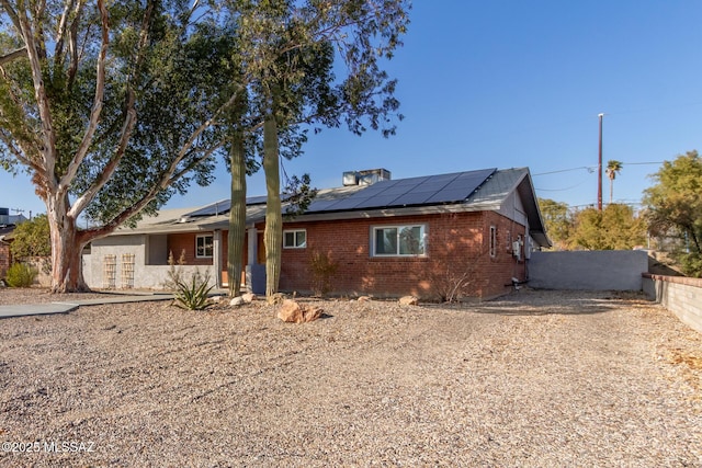 ranch-style house with roof mounted solar panels, fence, and brick siding