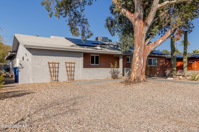 rear view of house featuring stucco siding, brick siding, and solar panels