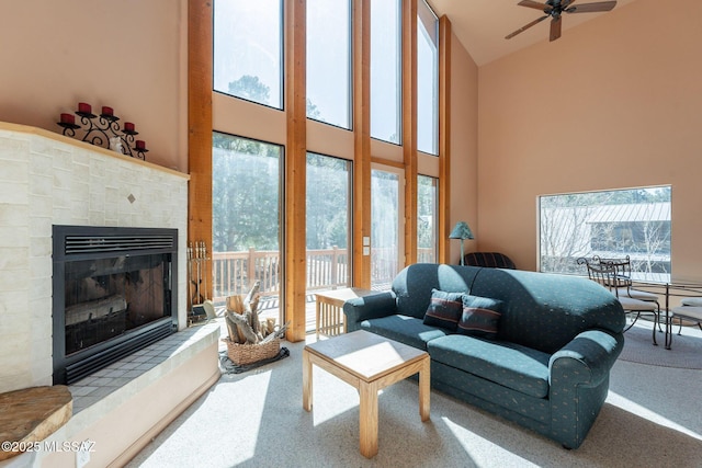 living room with ceiling fan, a glass covered fireplace, high vaulted ceiling, and carpet floors