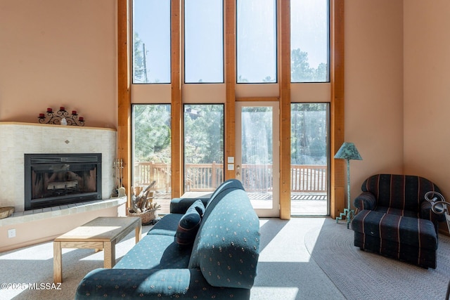 living room with carpet flooring, a healthy amount of sunlight, a tile fireplace, and a towering ceiling