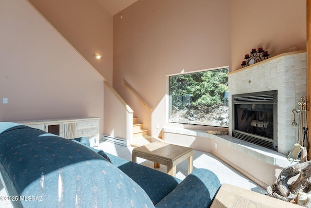 carpeted living room featuring stairs, a baseboard radiator, a fireplace with raised hearth, and high vaulted ceiling