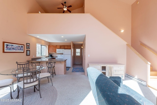 dining room with a towering ceiling, ceiling fan, light carpet, a baseboard radiator, and recessed lighting