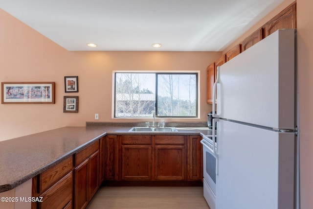 kitchen with white appliances, a sink, light wood-style floors, brown cabinets, and dark countertops