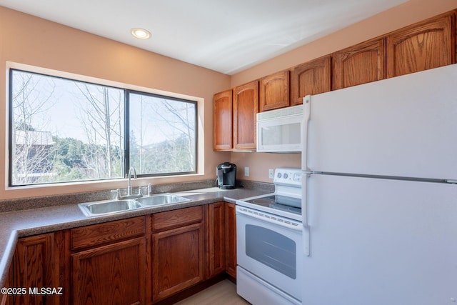 kitchen featuring dark countertops, brown cabinetry, a sink, and white appliances