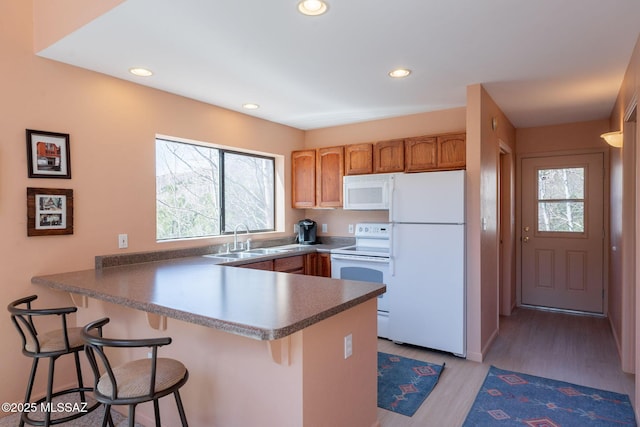 kitchen featuring recessed lighting, white appliances, light wood finished floors, a sink, and a peninsula