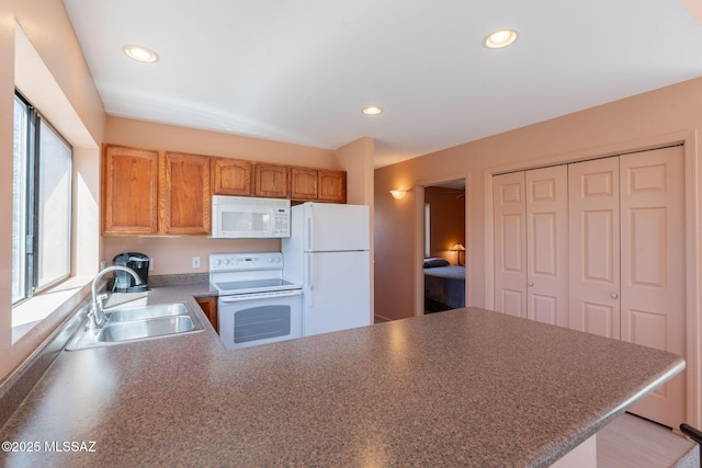 kitchen featuring white appliances, a peninsula, recessed lighting, and a sink