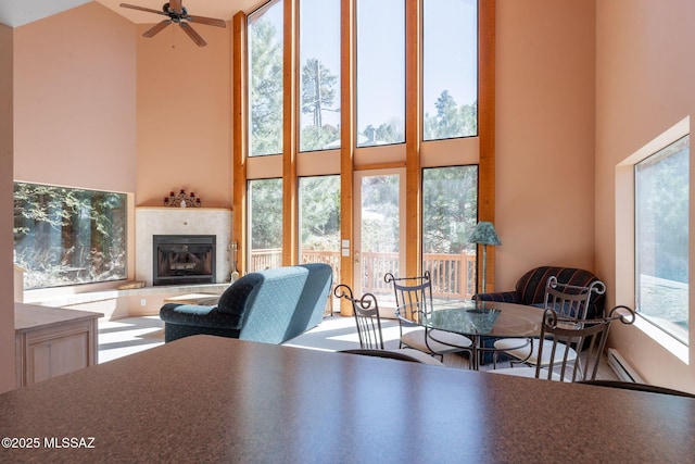 living area featuring a baseboard heating unit, a high ceiling, a ceiling fan, and a tile fireplace