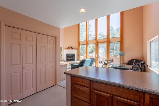 kitchen with light wood-style flooring, brown cabinets, a tiled fireplace, open floor plan, and recessed lighting