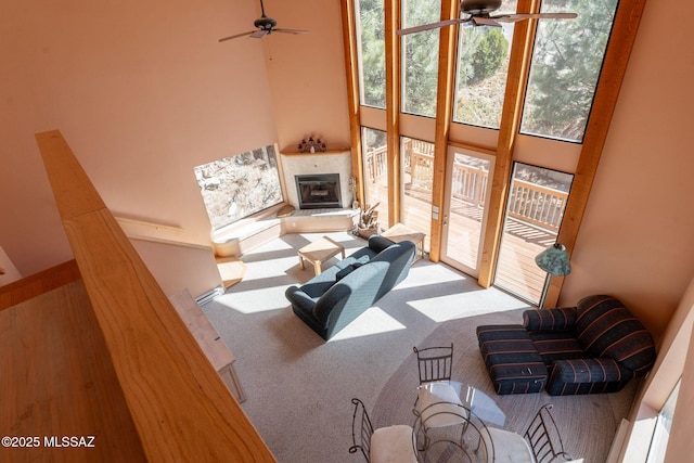 carpeted living area with a tiled fireplace, ceiling fan, and a high ceiling