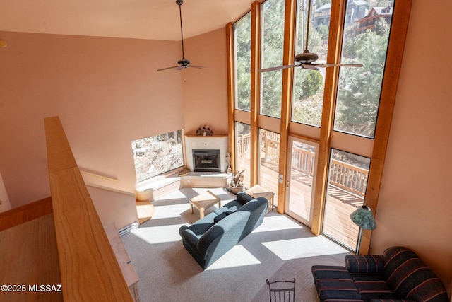 carpeted living area featuring ceiling fan, a high ceiling, and a glass covered fireplace