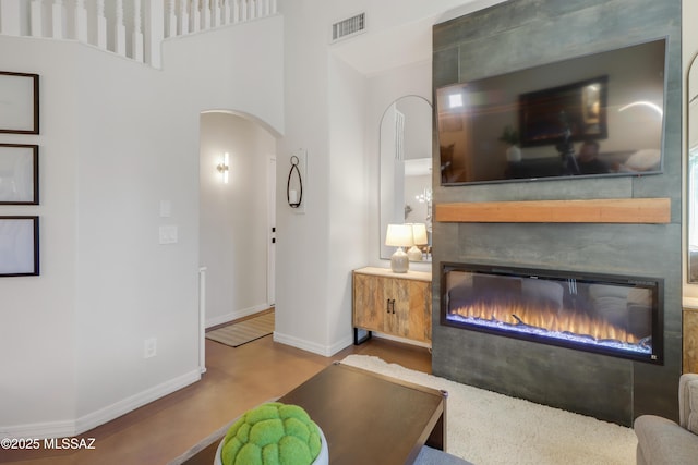 29 W Camino Rancho Viejo, Sahuarita, AZ 85629 - living room featuring arched walkways, a glass covered fireplace, baseboards, wood finished floors, and a towering ceiling