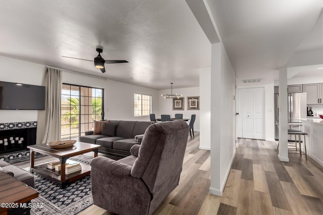living area with baseboards, light wood finished floors, visible vents, and ceiling fan with notable chandelier