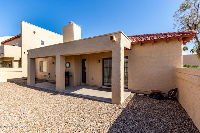 rear view of property featuring stucco siding, a tile roof, fence, a chimney, and a patio area