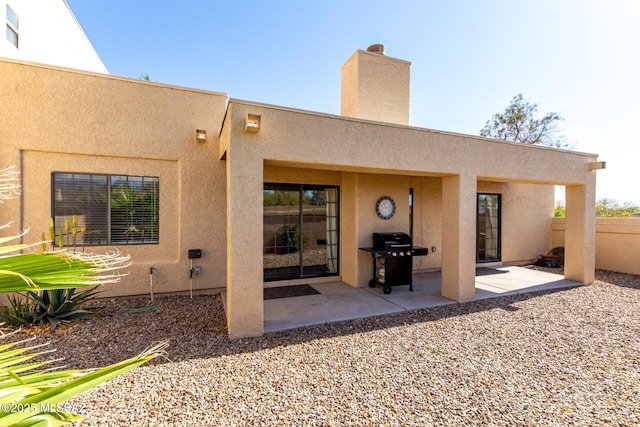 back of house with stucco siding, a chimney, and a patio
