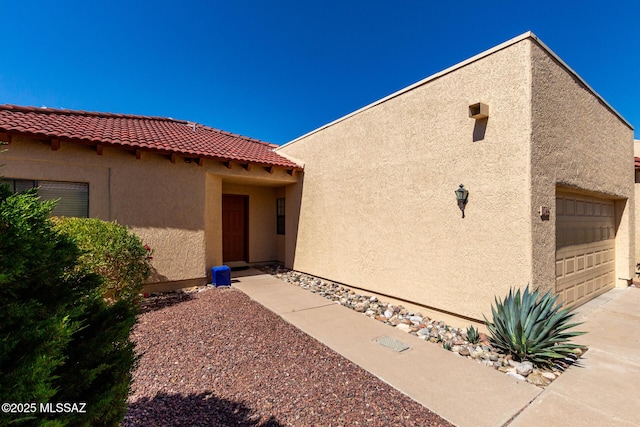 entrance to property featuring a tile roof, a garage, stucco siding, and driveway