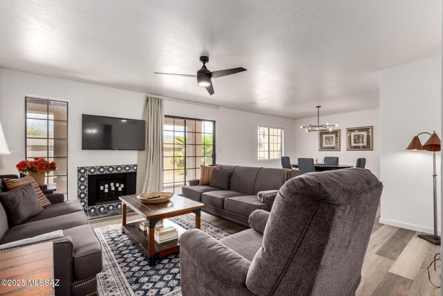 living area with light wood-style flooring, ceiling fan with notable chandelier, baseboards, and a tile fireplace