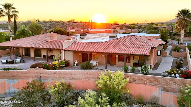 view of front of house with stucco siding, a patio area, a tiled roof, and a chimney