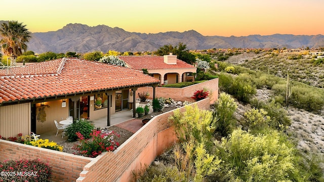 exterior space with a mountain view, a tiled roof, a patio area, and a chimney