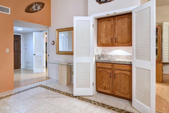 kitchen with a high ceiling, a sink, brown cabinetry, visible vents, and light tile patterned flooring