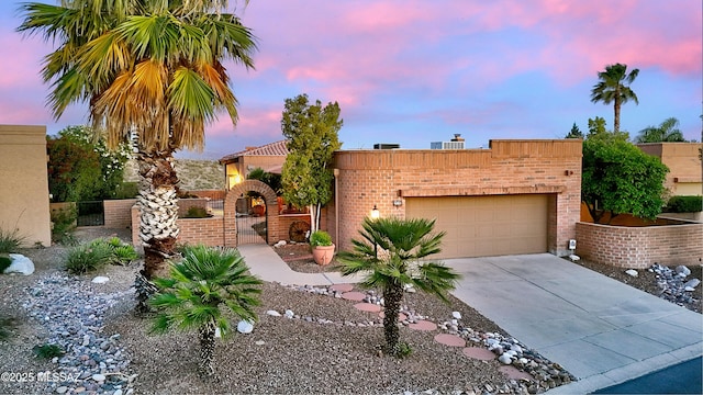 adobe home with brick siding, fence, a garage, concrete driveway, and a gate