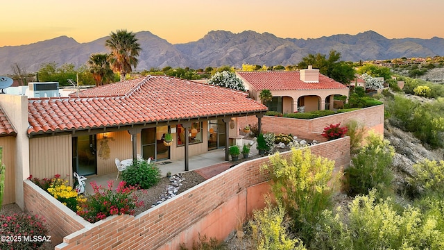 back of property at dusk featuring a patio area, a tiled roof, a mountain view, and fence