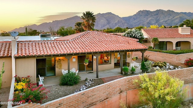 back of property at dusk featuring a patio, a tiled roof, and a mountain view