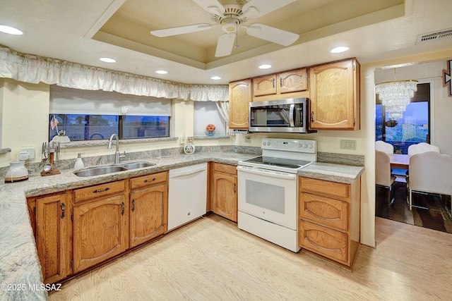 kitchen featuring a sink, white appliances, visible vents, a tray ceiling, and light wood-style floors