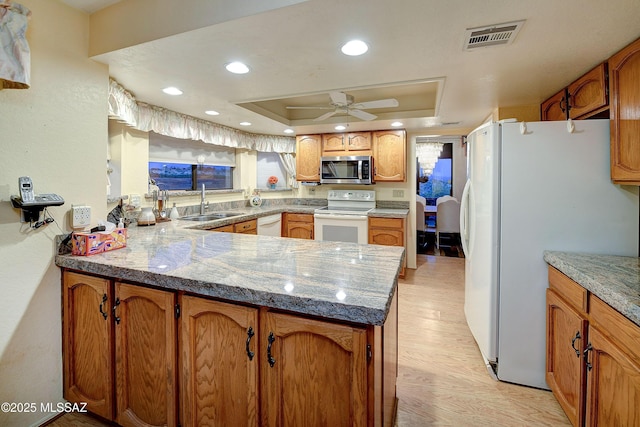 kitchen with a sink, a peninsula, white appliances, visible vents, and light wood-style flooring