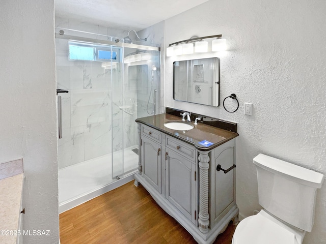 full bathroom featuring toilet, vanity, wood finished floors, a marble finish shower, and a textured wall