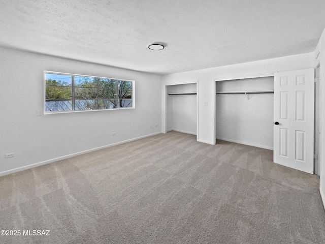 unfurnished bedroom featuring a textured ceiling, carpet, baseboards, and multiple closets