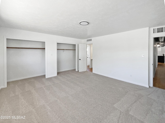 unfurnished bedroom with baseboards, visible vents, and two closets